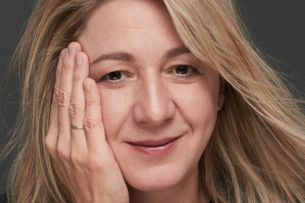 Eine blonde Frau mit Blick in die Kamera hält ihr Gesicht in ihrer rechten Hand