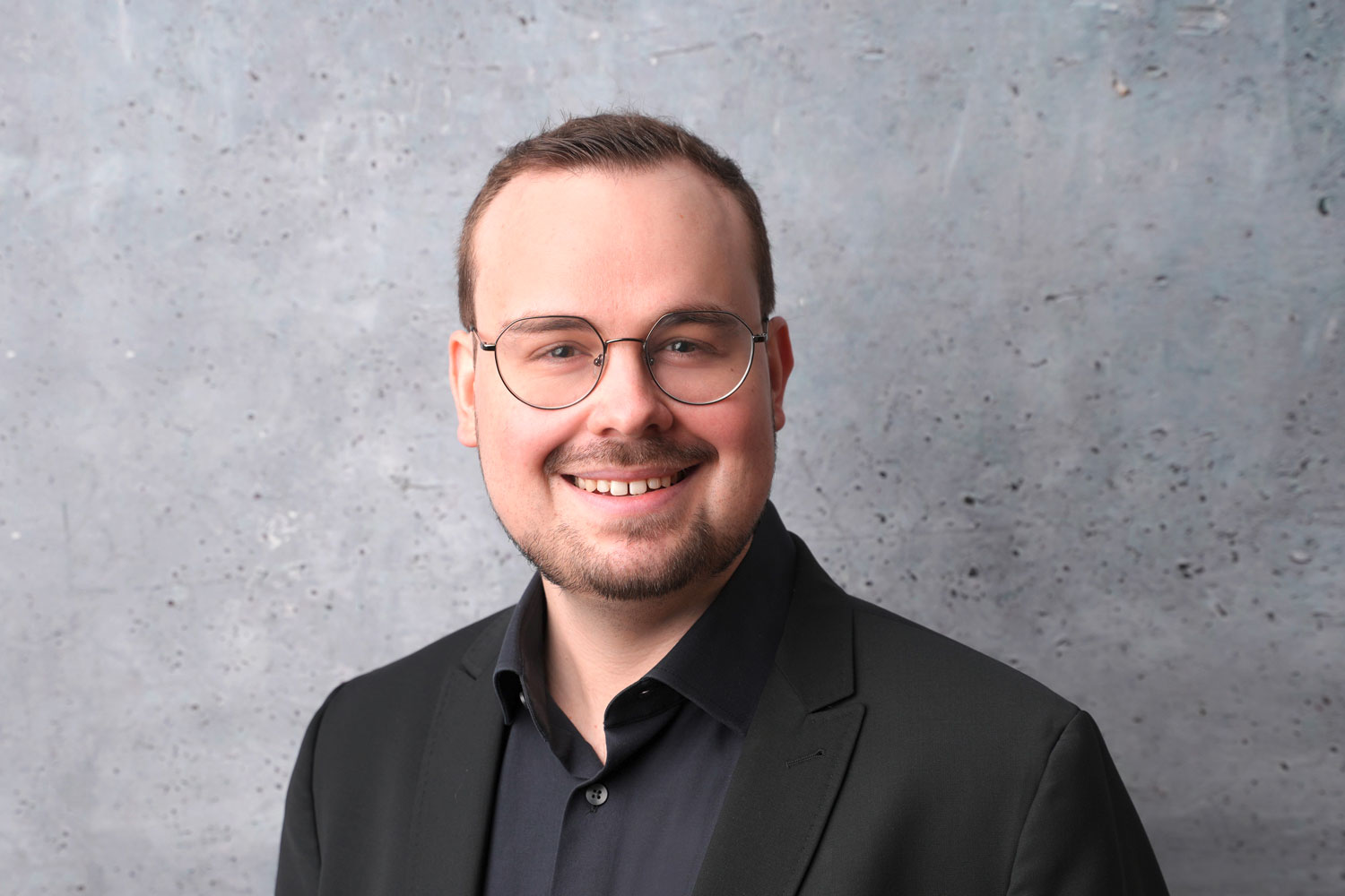 Portraitfoto eine freundlich lächelnden Herrn mit Brille vor grauem Hintergrund